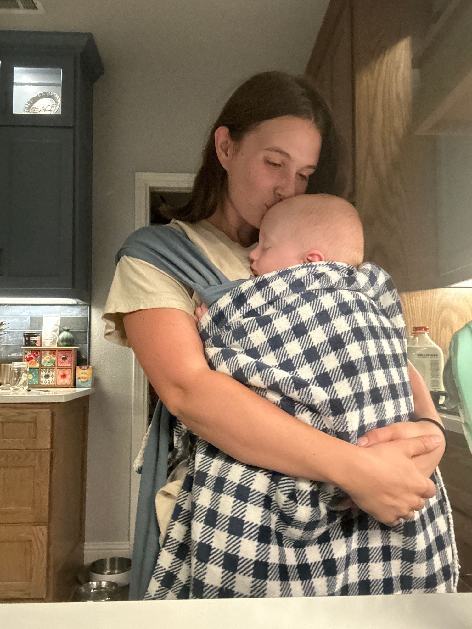 Tally kissing the head of her sleeping baby, who is wrapped against her chest in a carrier